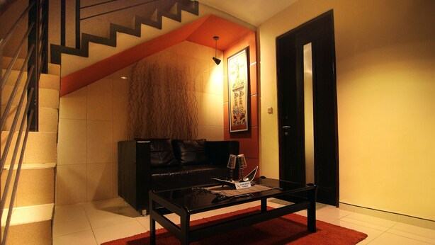 A modern living room with a staircase, a black sofa, a coffee table, and a red rug. - Puri Chorus Hotel (Yogyakarta)