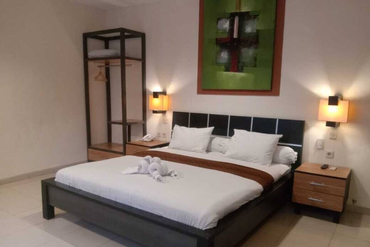 A modern hotel room with a large bed, two bedside tables, a wardrobe, and a painting on the wall.