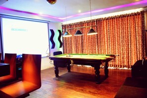 A billiards table with a projector screen, a pool table, and a patterned curtain in a room with wooden flooring and modern lighting. - The Rosedale Grand Nuwara Eliya (Nuwara Eliya)