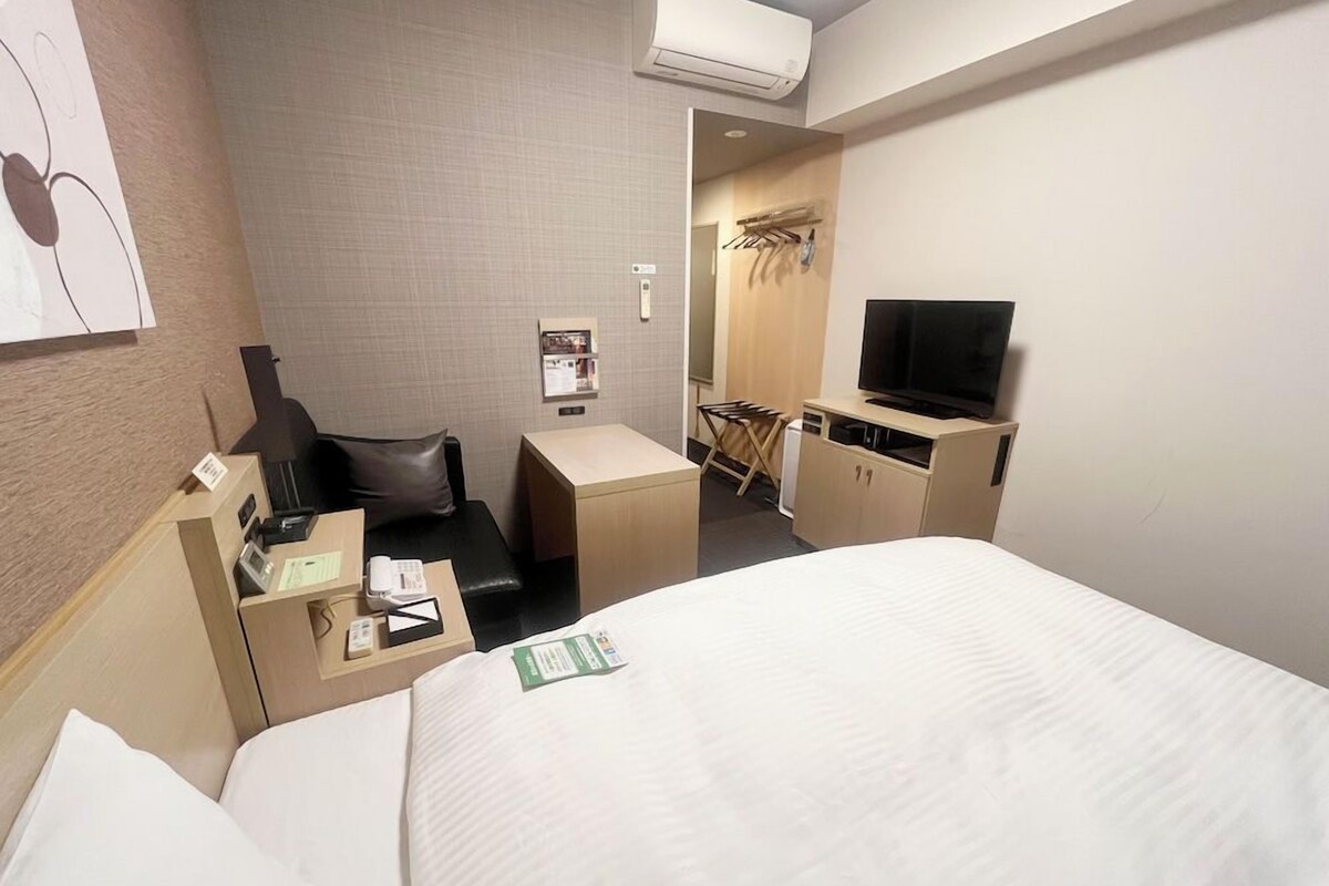 Una habitación de hotel con cama, escritorio con silla, televisión y un pequeño rincón de estar con mesa y sillas.