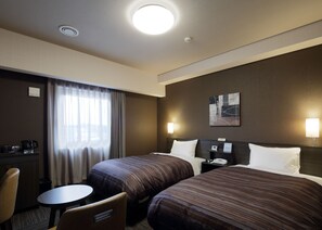 A hotel room with two beds, a desk, a chair, a small table, and a nightstand with a lamp.