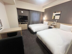 A hotel room with two beds, a desk, a TV, and a nightstand with a lamp.