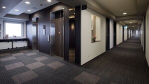 A long corridor with carpeted floors, a reception desk, and a wall-mounted elevator. - Hotel Route Inn Ube (Ube)