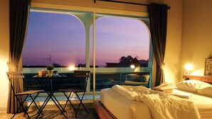 A hotel room with a balcony, a bed, a desk, and a view of the sunset. - Sattahiptale Boutique Guest House & Hostel (Sattahip)