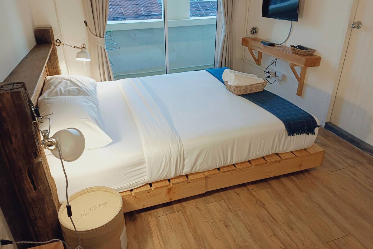 A bedroom with a wooden bed, a TV on the wall, and a window with a view of buildings.