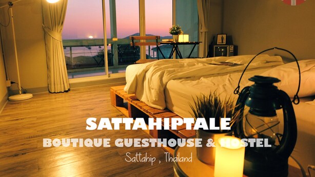 A room with a bed, a table with a plant, a lantern, and a view of the sunset through large windows. - Sattahiptale Boutique Guest House & Hostel (Sattahip)