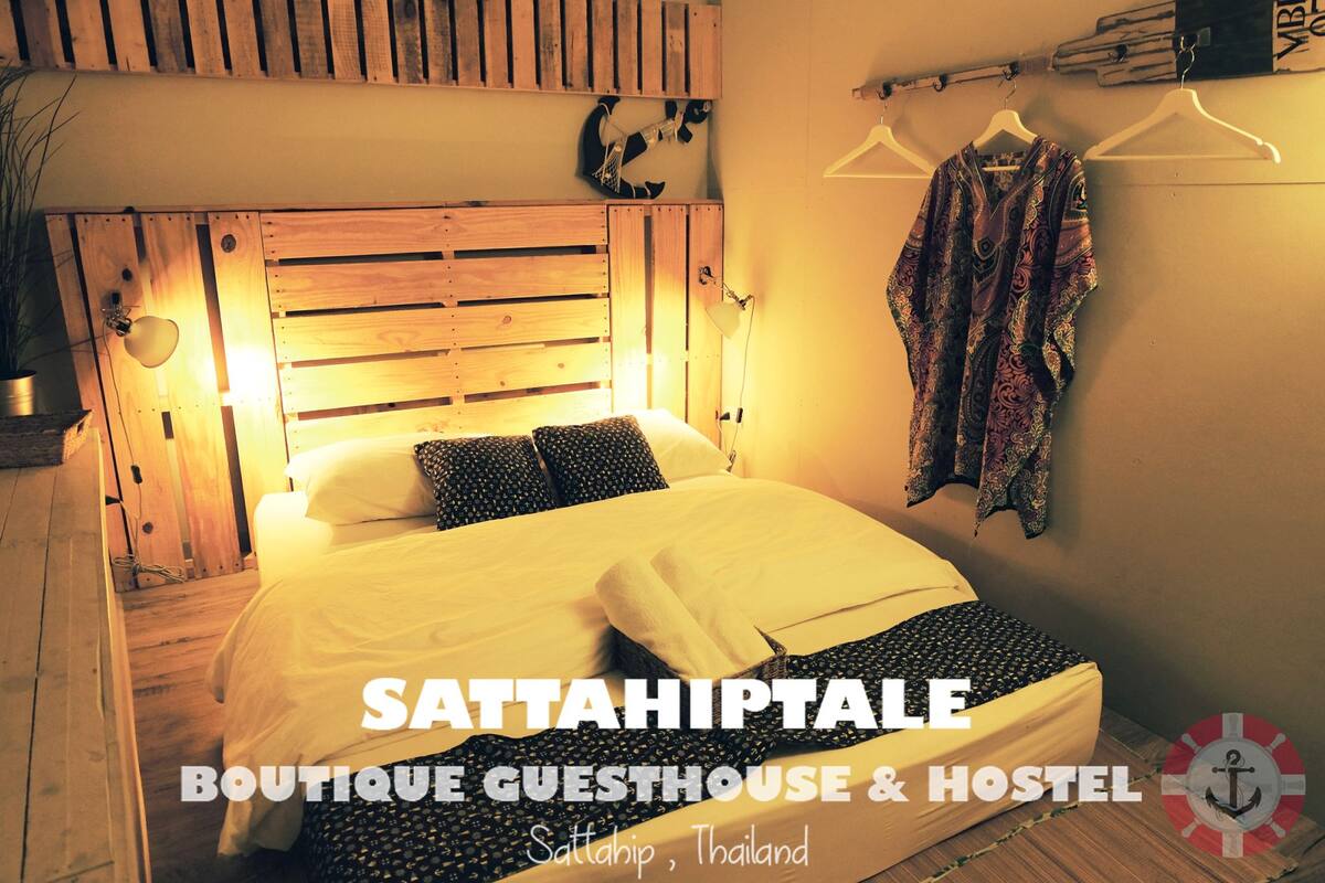 A bed with a wooden headboard, a hanging garment, and a wall-mounted light fixture in a room with a simple, rustic design.