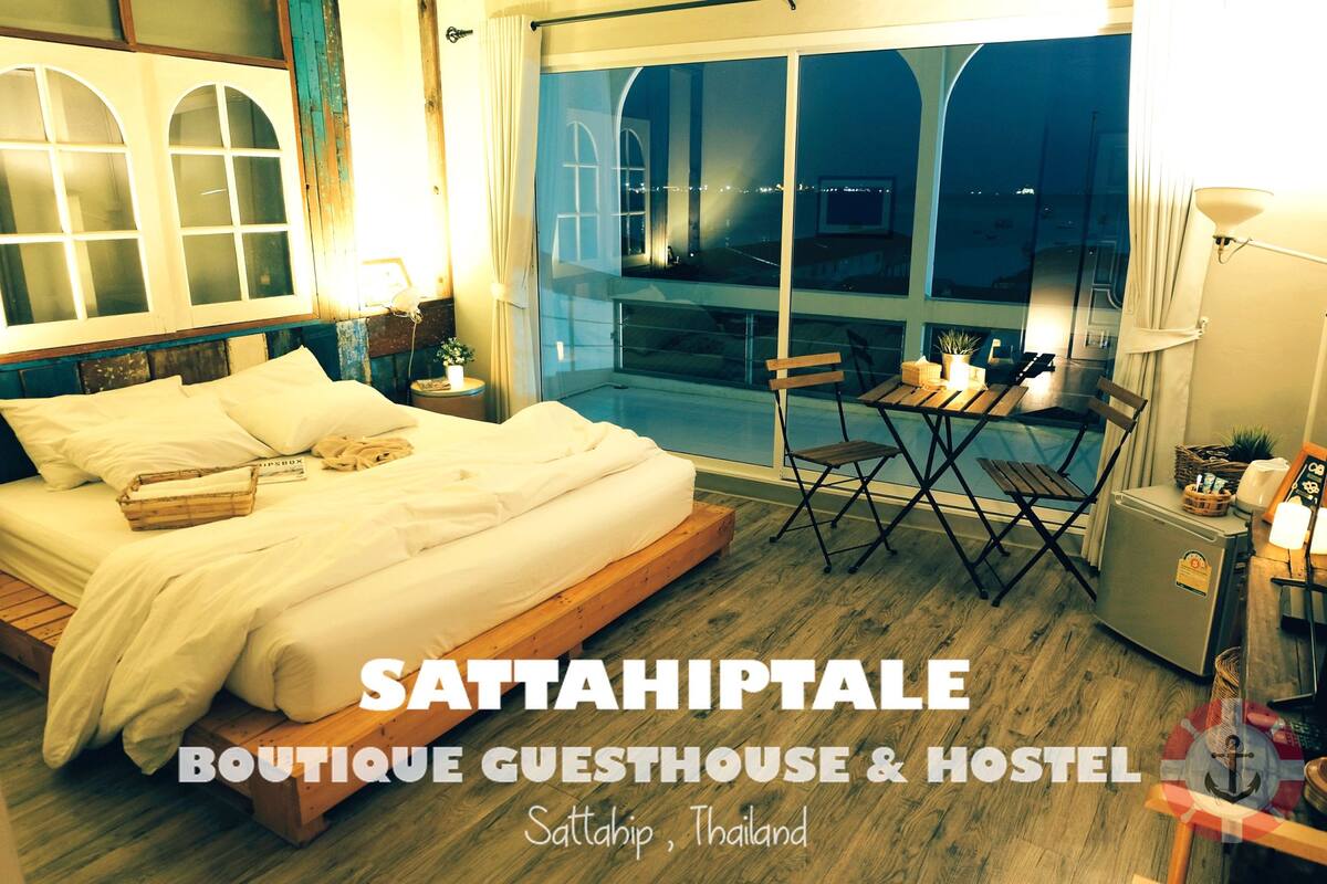 A guesthouse with a bed, a small table, and a chair near a window overlooking the city.