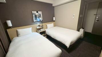 A hotel room with two beds, a nightstand, a lamp, a trash bin, and a door.