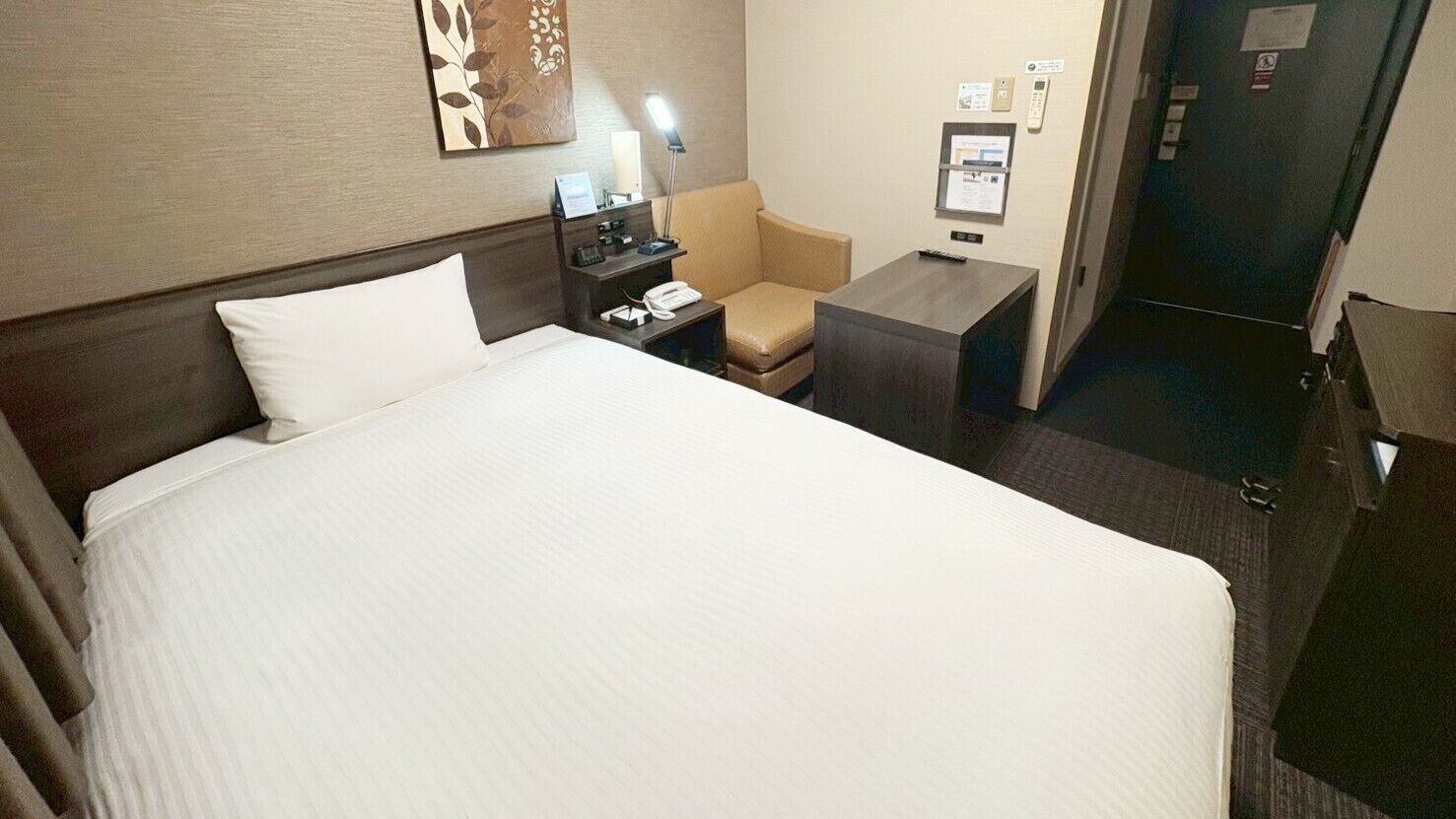 Ein Hotelzimmer mit einem großen Bett, einem Schreibtisch, einem Stuhl, einem Nachttisch und einer Lampe.