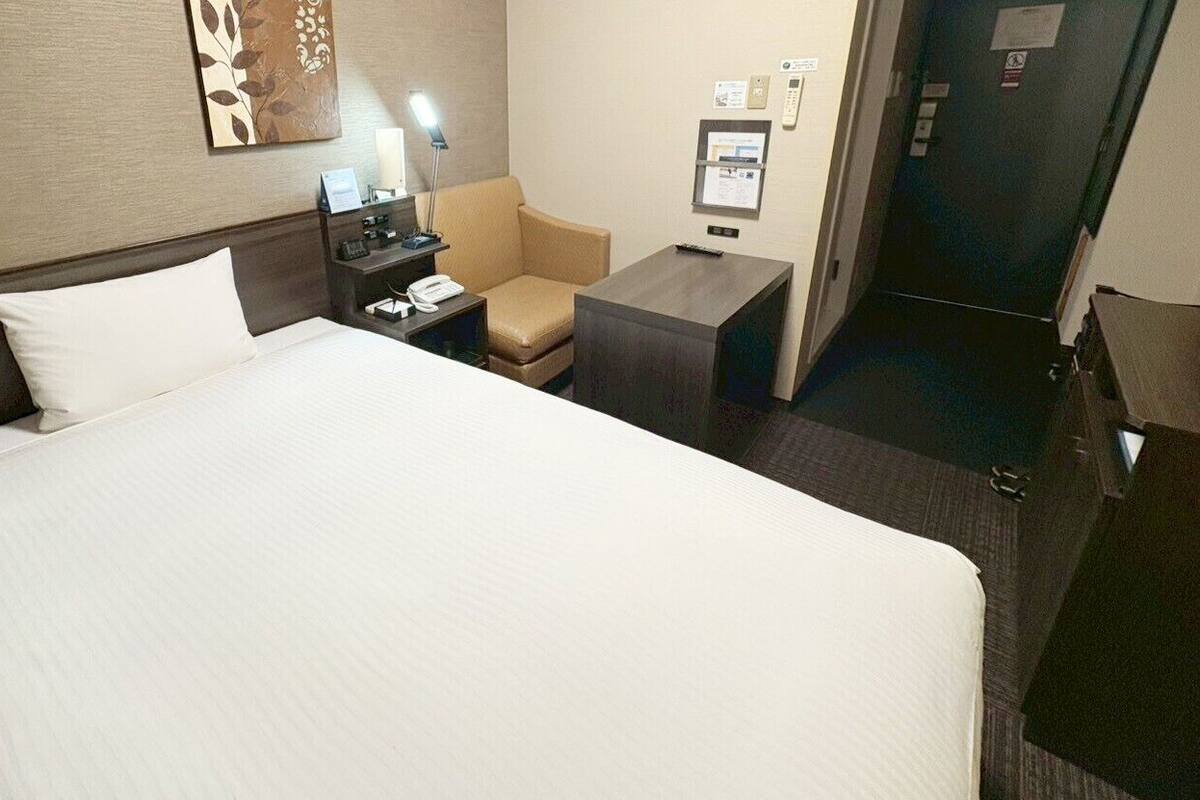 Une chambre d’hôtel avec un grand lit, un bureau, une chaise, une table de chevet et une lampe.