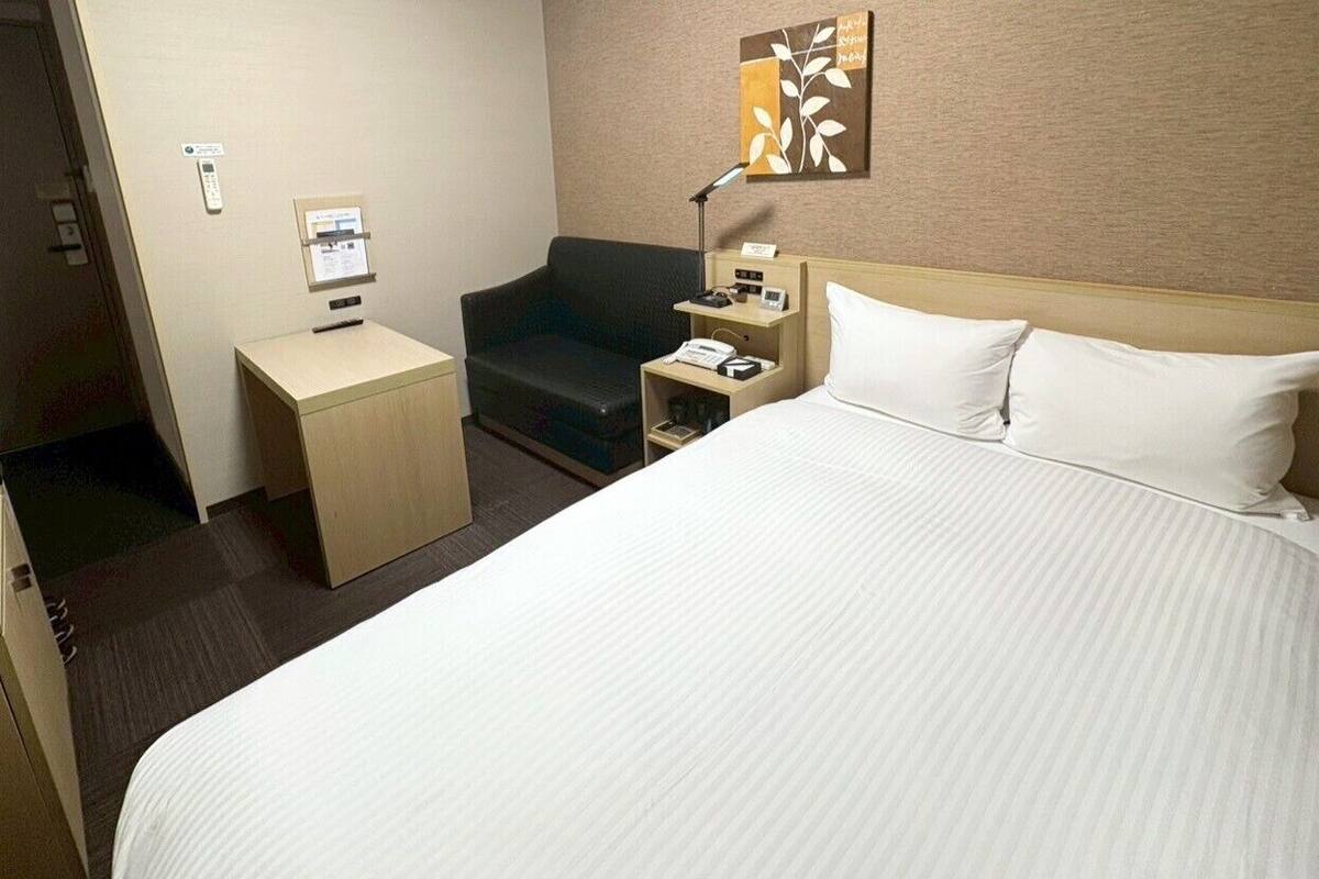 Une chambre d’hôtel avec un grand lit, un bureau, une chaise, une table de chevet, une lampe et un téléphone fixé au mur.