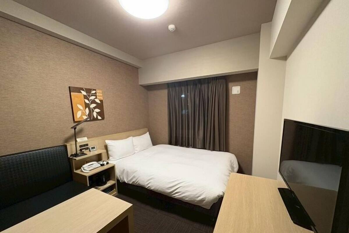 Une chambre d’hôtel comprenant un lit, un bureau, une chaise, une télévision, une table de chevet et une œuvre d’art accrochée au mur.