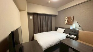 Une chambre d’hôtel équipée d’un lit, d’un bureau, d’une chaise, d’une télévision et d’une table de chevet avec une lampe.