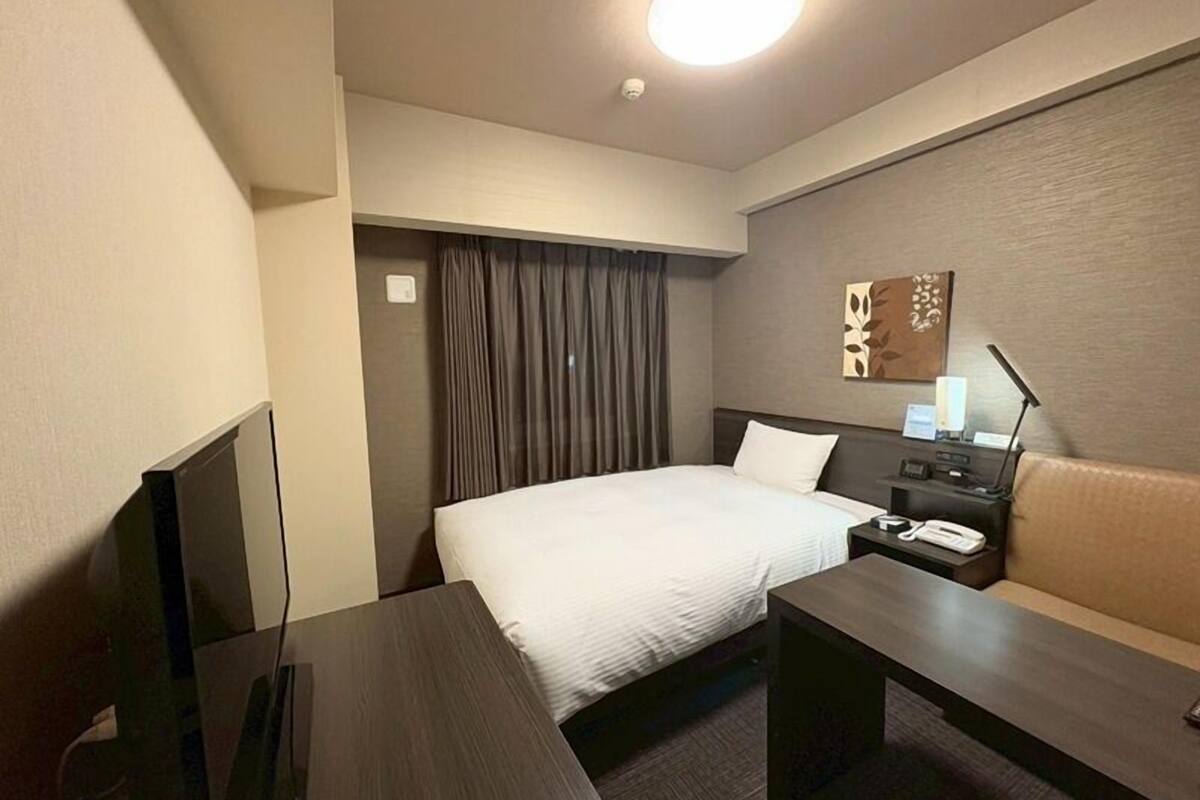Une chambre d’hôtel équipée d’un lit, d’un bureau, d’une chaise, d’une télévision et d’une table de chevet avec une lampe.