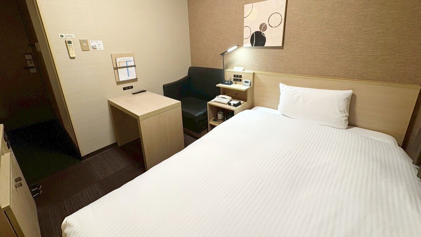 Ein Hotelzimmer mit einem großen Bett, einem Schreibtisch, einem Sessel, einem Nachttisch und einem an der Wand befestigten Telefon.