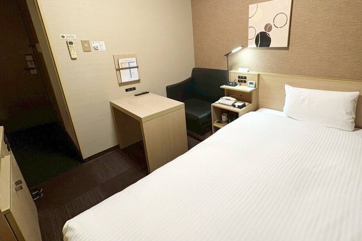 Une chambre d’hôtel avec un grand lit, un bureau, une chaise, une table de chevet et un téléphone fixé au mur.