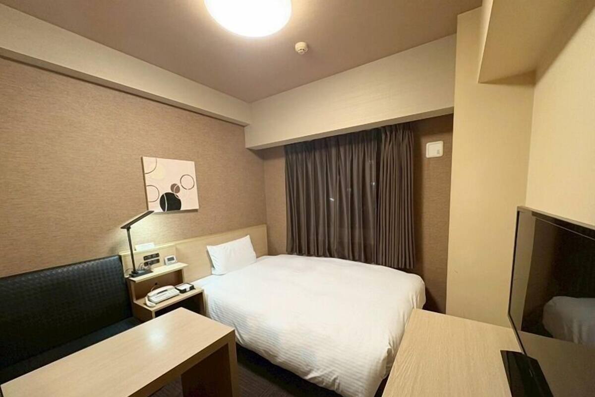 Une chambre d’hôtel avec un lit, un bureau, une chaise, une table de chevet, une lampe, un téléviseur et un tableau au mur.