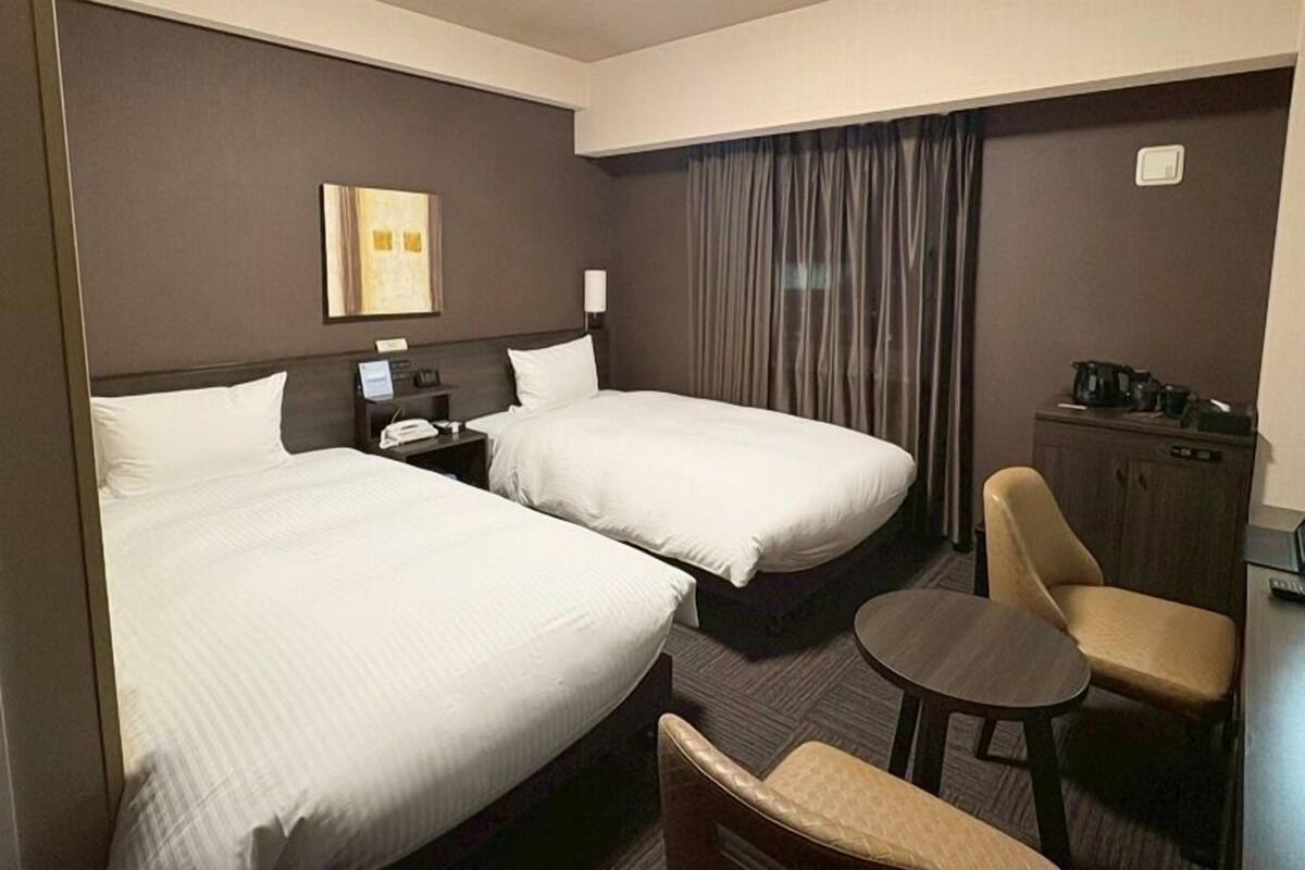 Une chambre d’hôtel avec deux lits, un bureau, une chaise, une petite table et un placard.