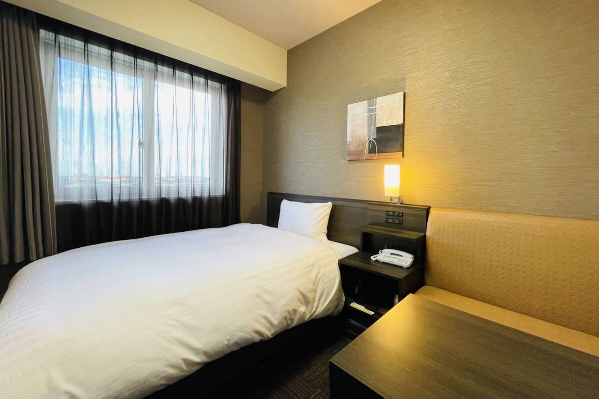 A hotel room with a large bed, a bedside table with a lamp, a small table, and a nightstand with a phone.