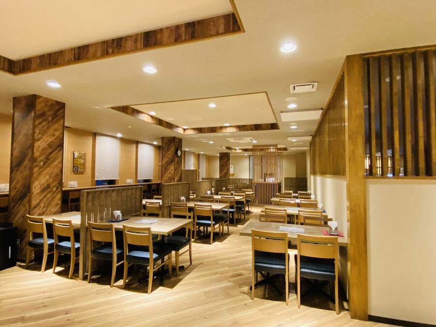 A spacious restaurant with wooden flooring, multiple tables and chairs, and a modern interior design.