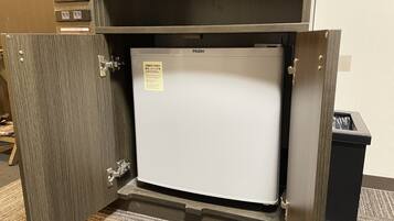 Un refrigerador compacto en un cuarto de servicio con puerta de madera y manija de metal.