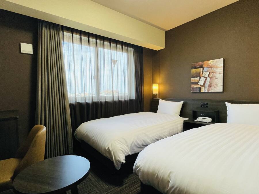 Een hotelkamer met twee bedden, een bureau, een stoel en een raam met gordijnen.