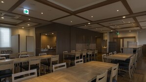Un comedor amplio con varias mesas y sillas de madera, una zona de cocina al fondo y un techo con iluminación empotrada.