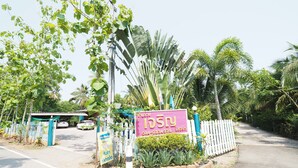 A gated entrance with a signboard, surrounded by lush greenery and palm trees.