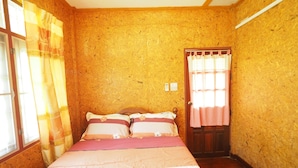 A bedroom with a wooden wall, a bed with a pink and white bedspread, two pillows, a wooden door, and a window with curtains.