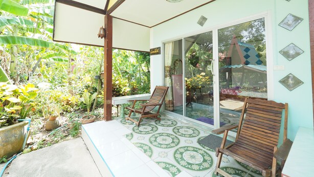 A covered patio with two wooden chairs, a potted plant, and a patterned floor.