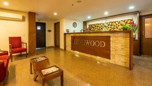 Un comptoir d’accueil avec un revêtement en bois et l’inscription « ROSEWOOD ». On y trouve deux chaises rouges et une table en bois sur laquelle est posé un magazine.