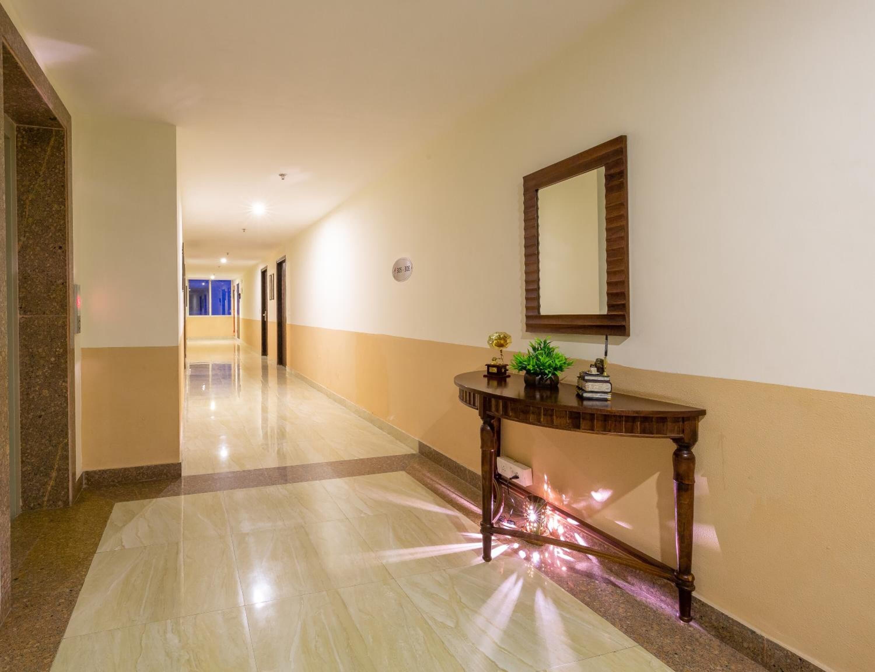 Un couloir d’hôtel avec un sol en marbre, une console en bois surmontée d’un miroir et une porte au fond.