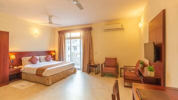 A hotel room with a large bed, a desk, a chair, a TV, and a ceiling fan.