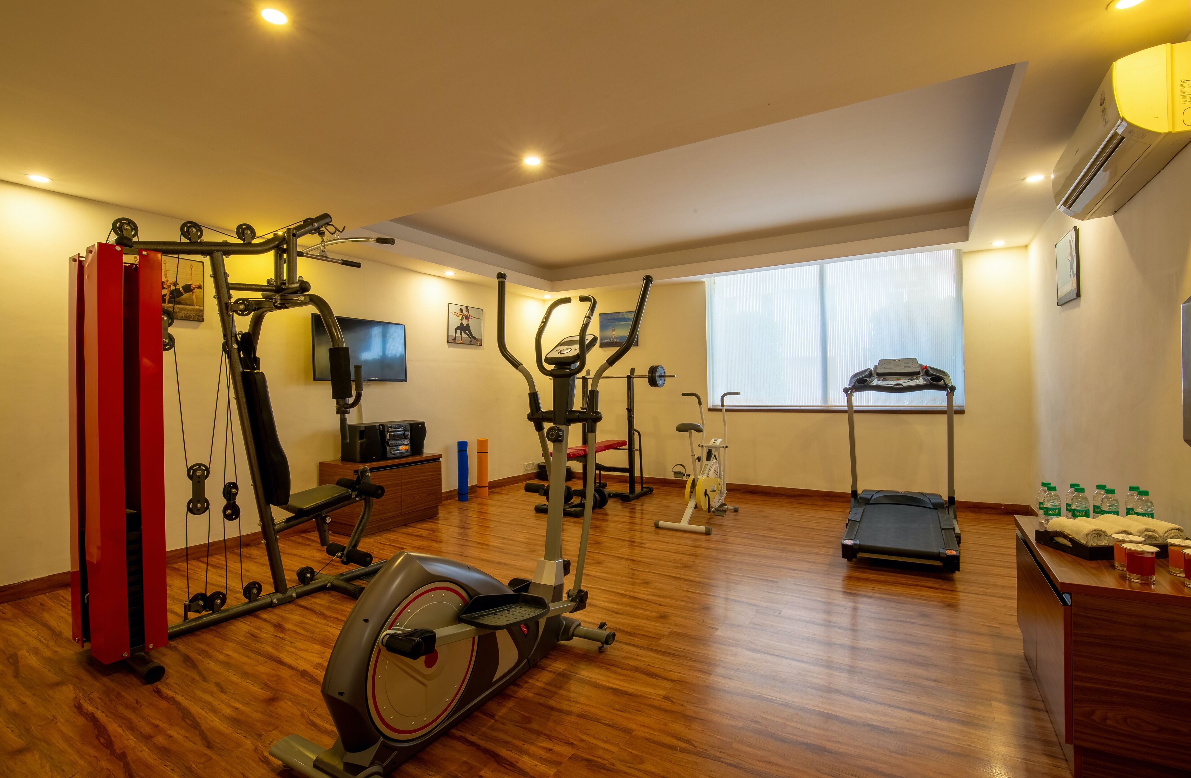Un gimnasio en casa con diferentes equipos de ejercicio, una cinta de correr y una ventana con persianas.