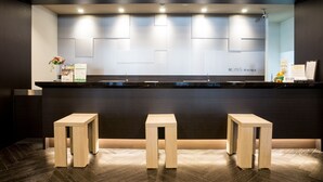 A reception area with a dark reception desk, three wooden stools, and a wall-mounted sign that reads "ROUTE IN N HOTELS". - Hotel Route Inn Fujichuokoen Higashi (Fuji)