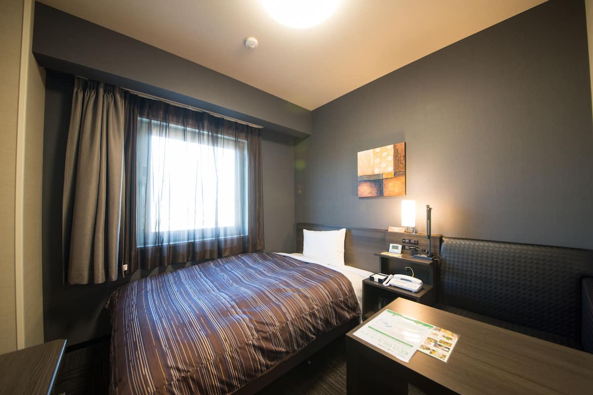 A hotel room with a large bed, a desk, a nightstand, a lamp, and a painting on the wall.
