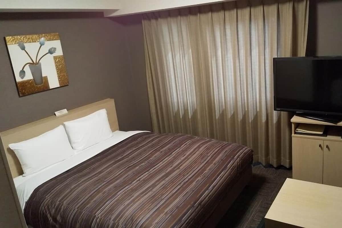 A hotel room with a bed, a television, a desk, and a painting on the wall.