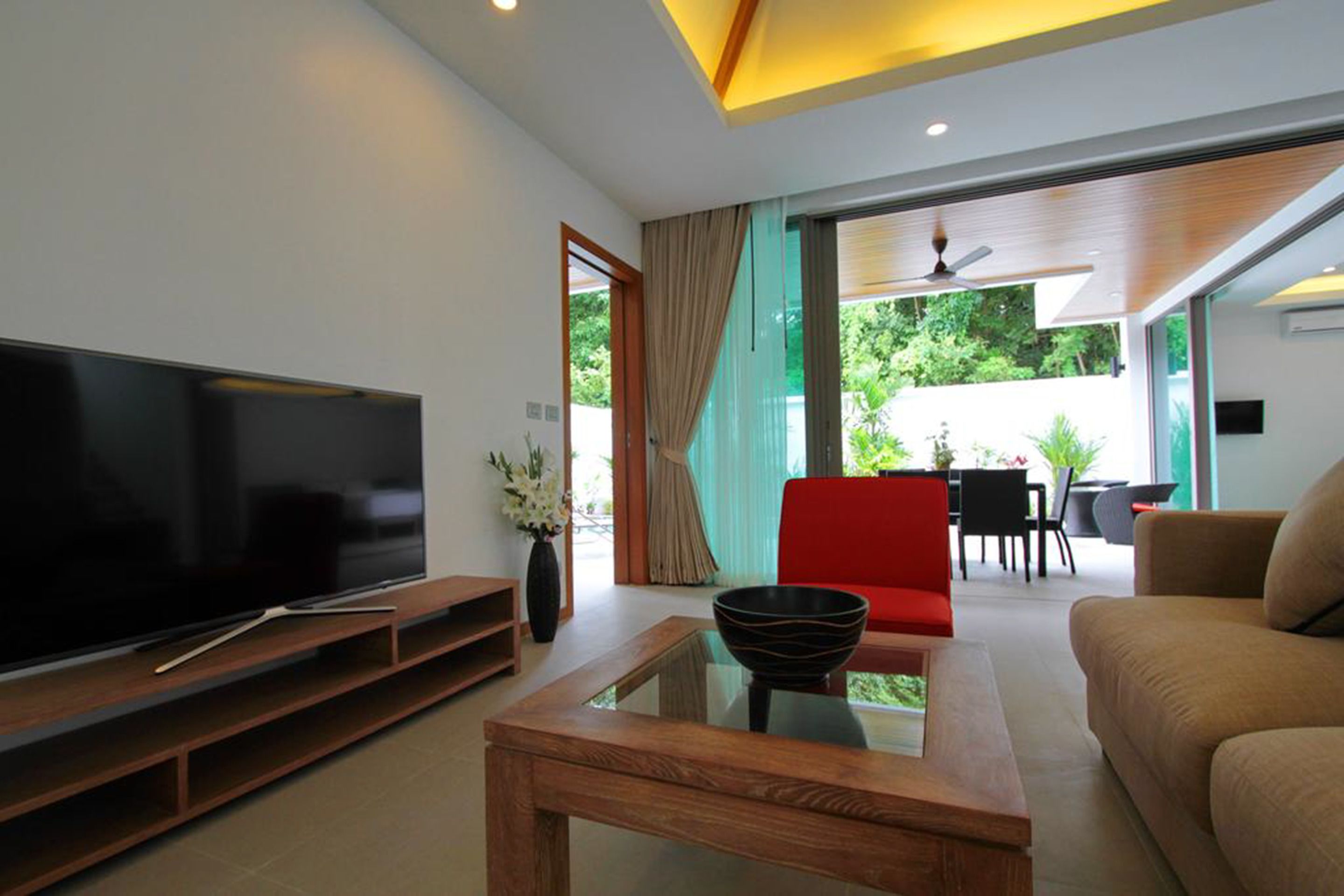 A modern living room with a flat-screen TV, a glass coffee table, and a red chair.