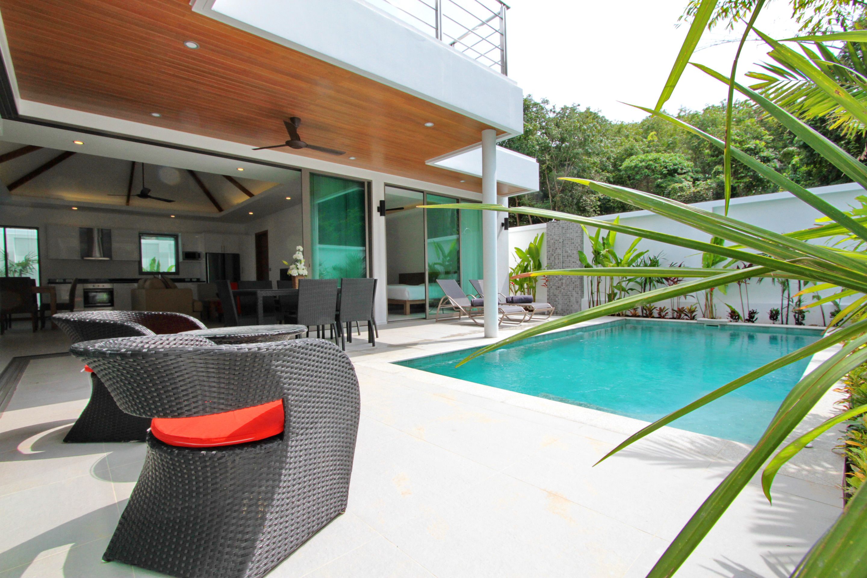 A modern outdoor pool area with wicker furniture and a view of the surrounding greenery.