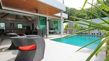 A modern outdoor pool area with wicker furniture and a view of the surrounding greenery.
