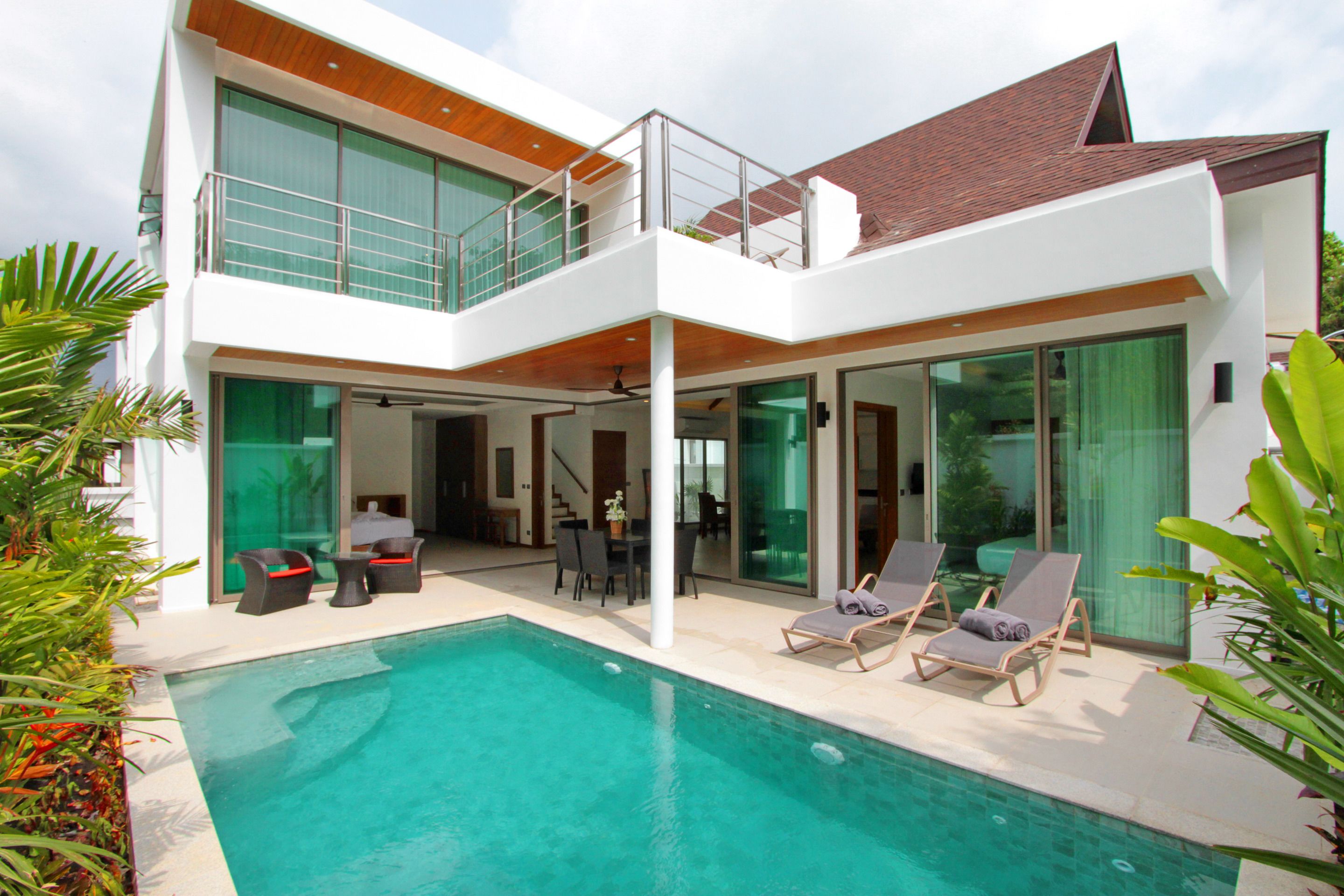 Una casa moderna de dos pisos con piscina, mobiliario exterior y ventanas amplias.