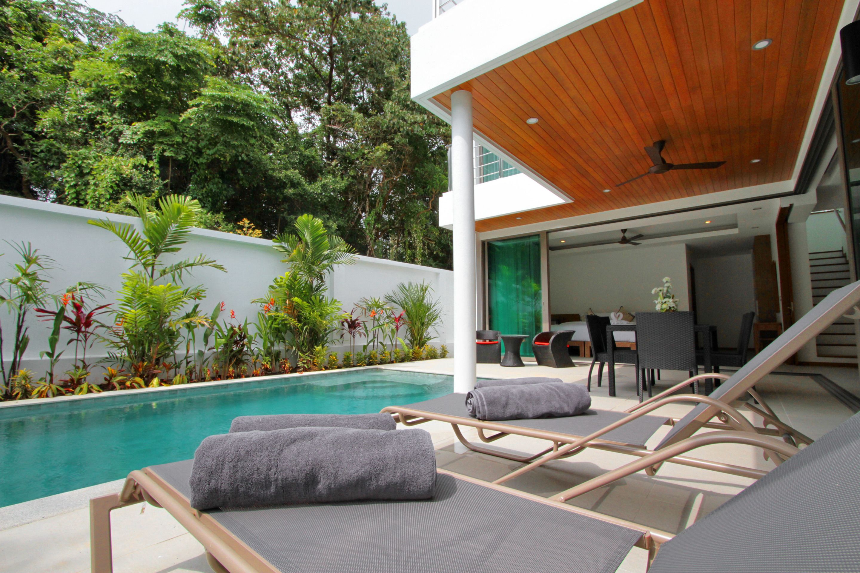 Un espace piscine extérieur moderne, doté de chaises longues et d’un coin repas.
