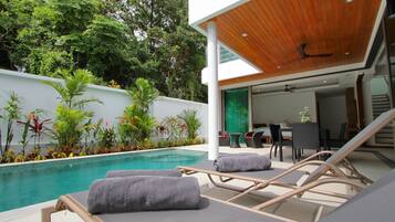 Un espace piscine extérieur moderne, doté de chaises longues et d’un coin repas.