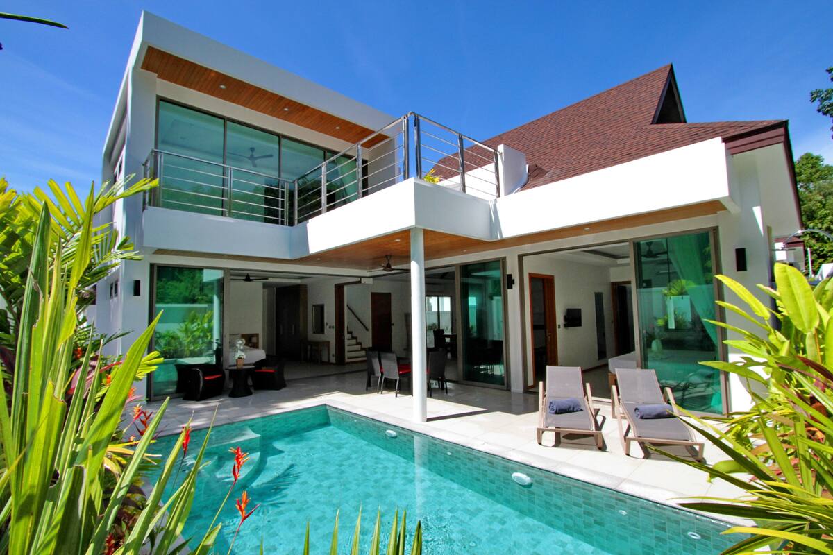 Ein modernes, zweistöckiges Haus mit Swimmingpool, Außenbereich zum Sitzen und großen Fenstern.