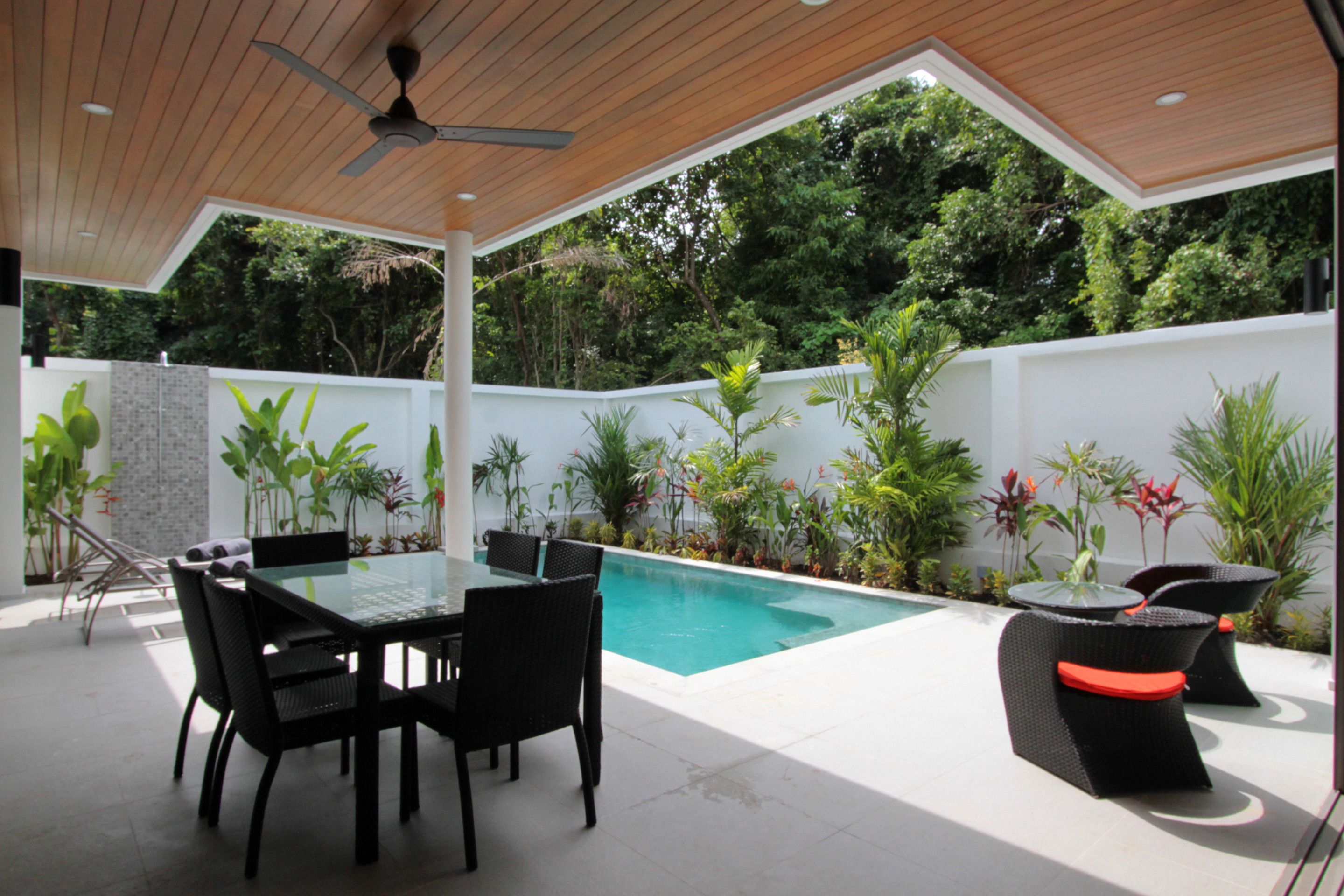 Une terrasse extérieure moderne, dotée d’une table et de chaises à plateau en verre, d’une piscine et d’une végétation luxuriante.