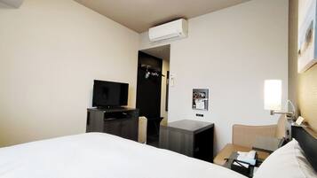 A hotel room with a bed, a desk, a television, an air conditioner, a nightstand, and a wall-mounted light.