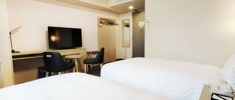 Habitación de hotel con dos camas, un escritorio con silla, televisor y aire acondicionado.