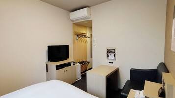A hotel room with a bed, a desk, a chair, a television, a wardrobe, and an air conditioning unit.