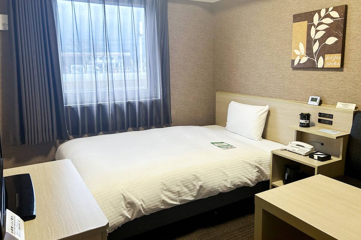 Ein Hotelzimmer mit Bett, Nachttisch und Schreibtisch mit Telefon und Kaffeemaschine.